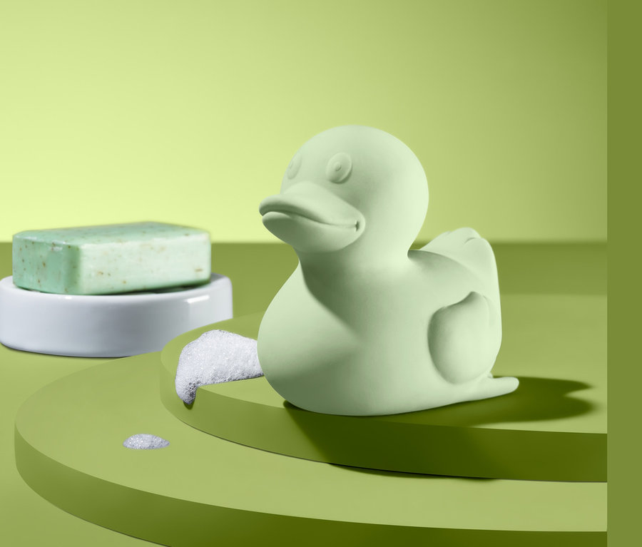 Zielona kaczuszka do kąpieli i zielone mydło na białej podstawce.