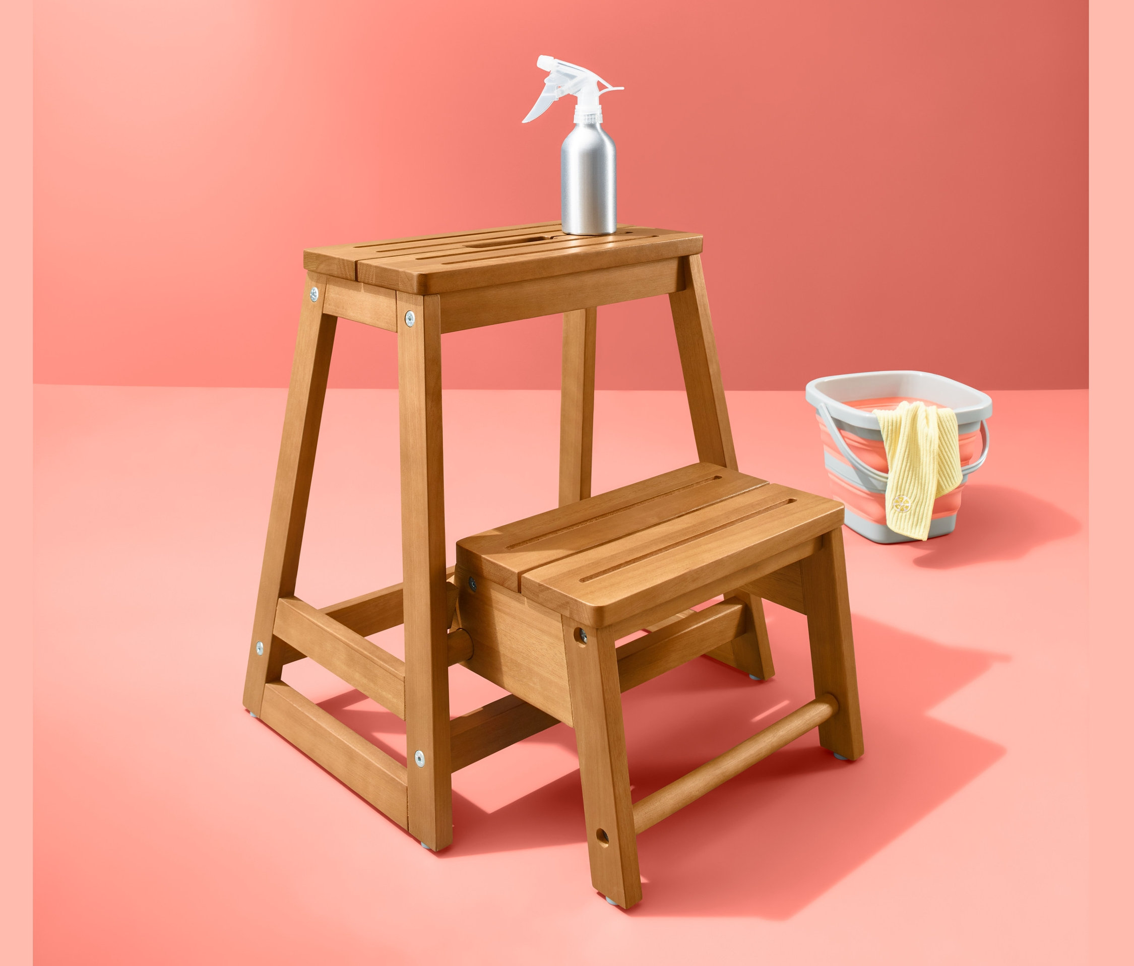 Drewniany składany stołek ze spryskiwaczem i wiadrem na koralowym tle.