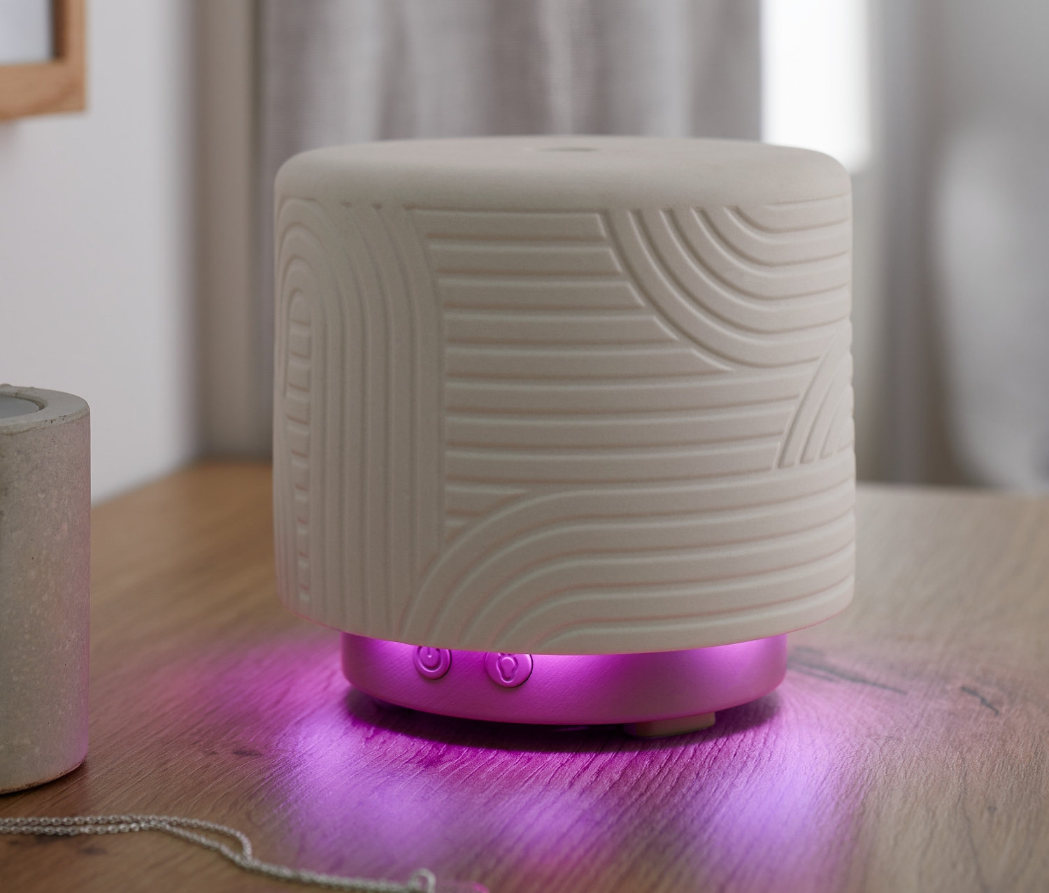 Biały dyfuzor zapachowy z geometrycznym wzorem i fioletowym podświetleniem na drewnianym stole.