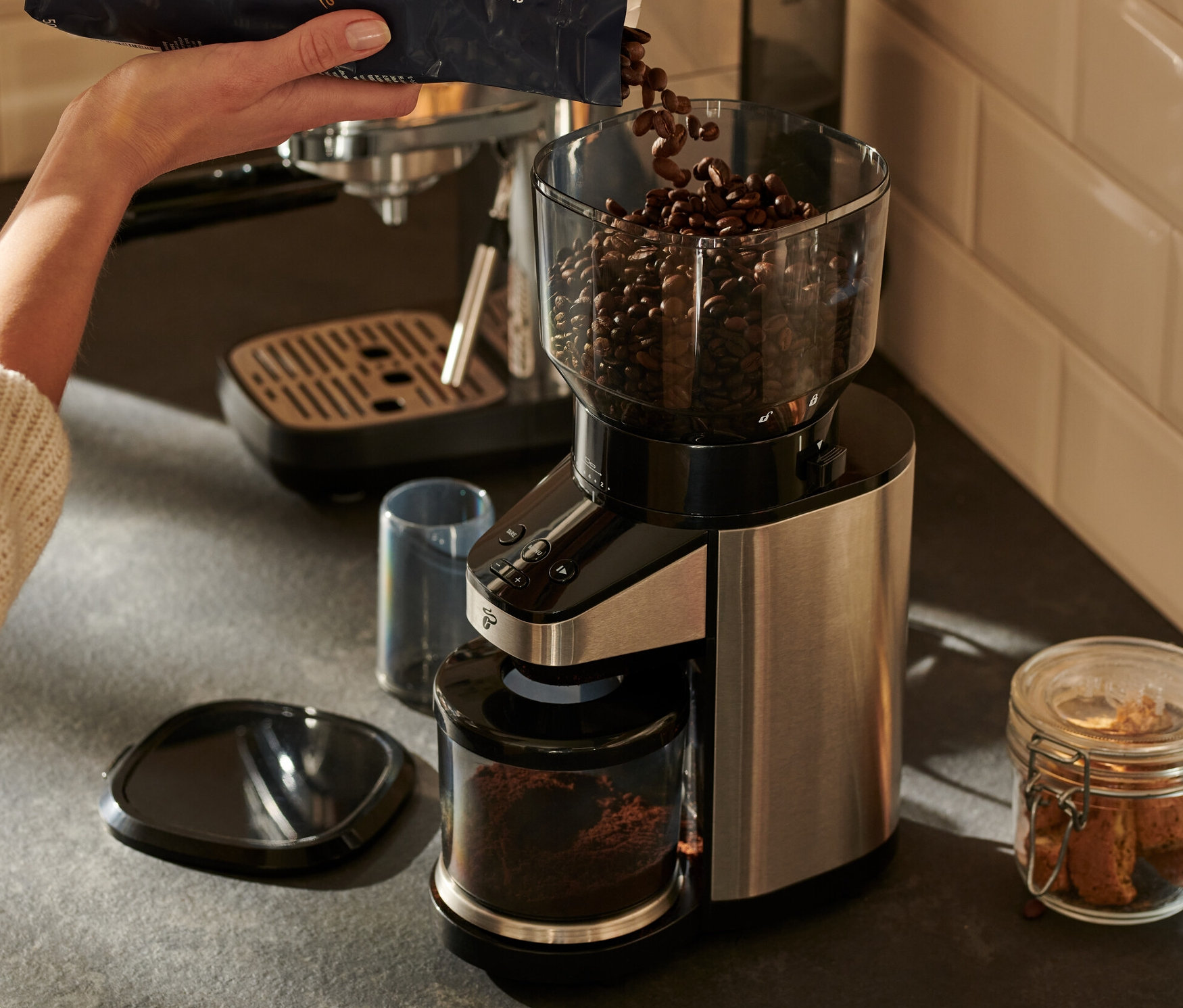 Kobieta wsypuje ziarna kawy do elektrycznego młynka do kawy z wagą.