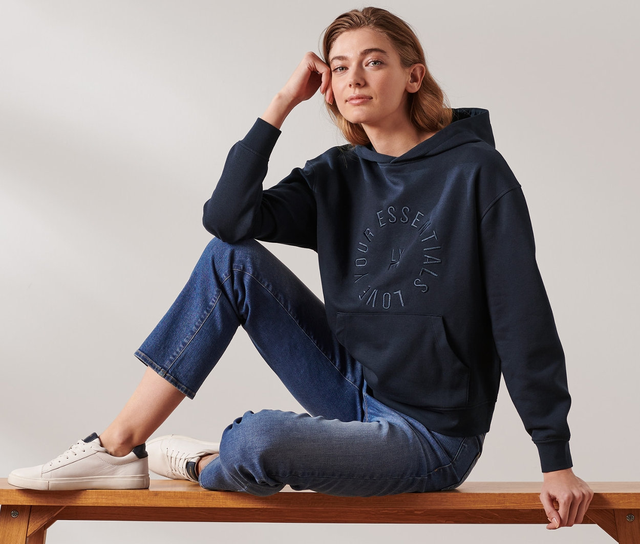 Kobieta siedzi na ławce, ubrana w granatową bluzę z kapturem.