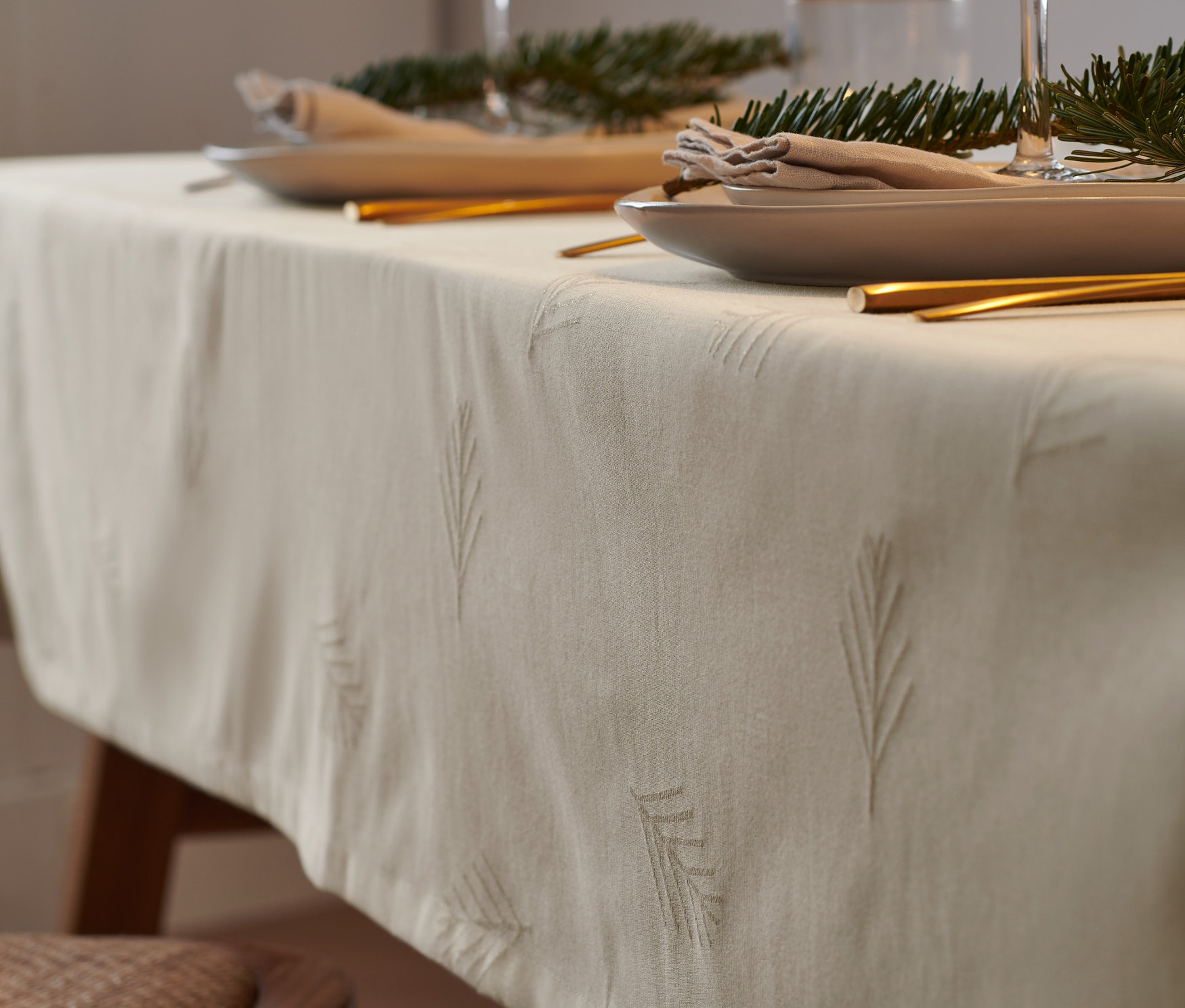 Zbliżenie stołu z obrusem żakardowym w kolorze złamanej bieli o standardowej wielkości, talerzami, sztućcami i szklankami.
