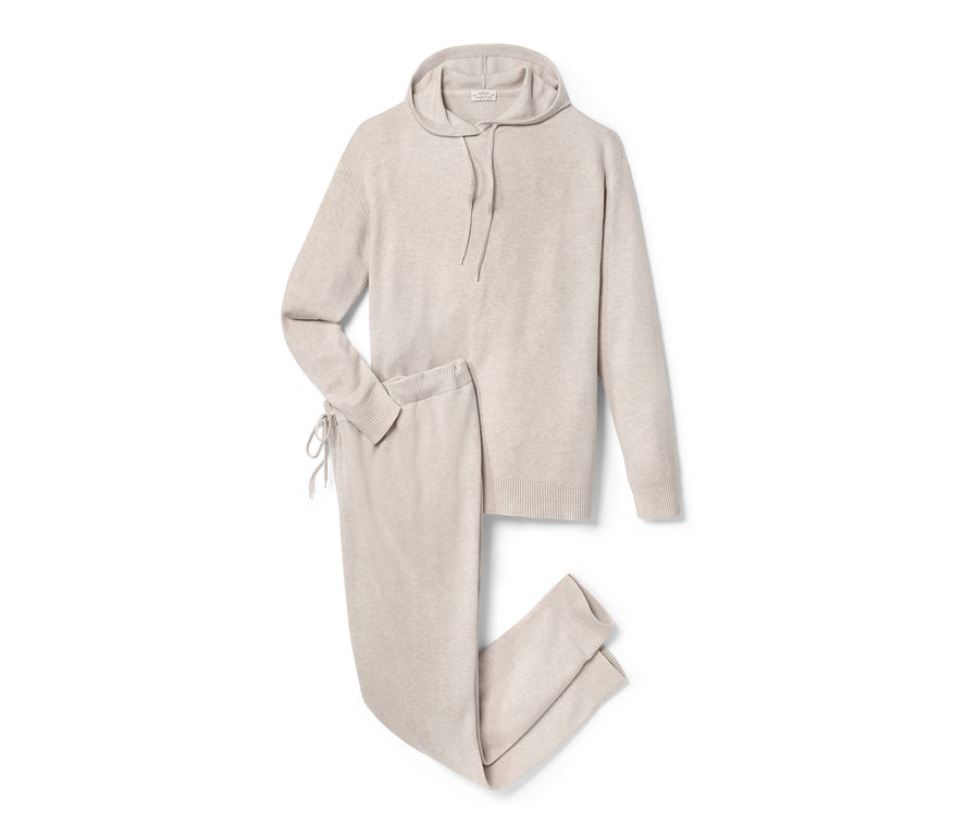 Beżowy dres ciążowy z bluzą z kapturem i spodniami leży na białym tle.