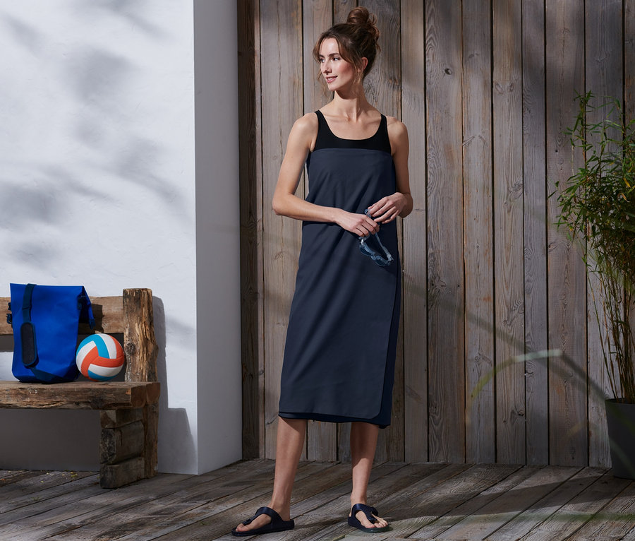 Kobieta trzyma okulary i ma na sobie turystyczny ręcznik kąpielowy XL, ok. 100 x 180 cm.