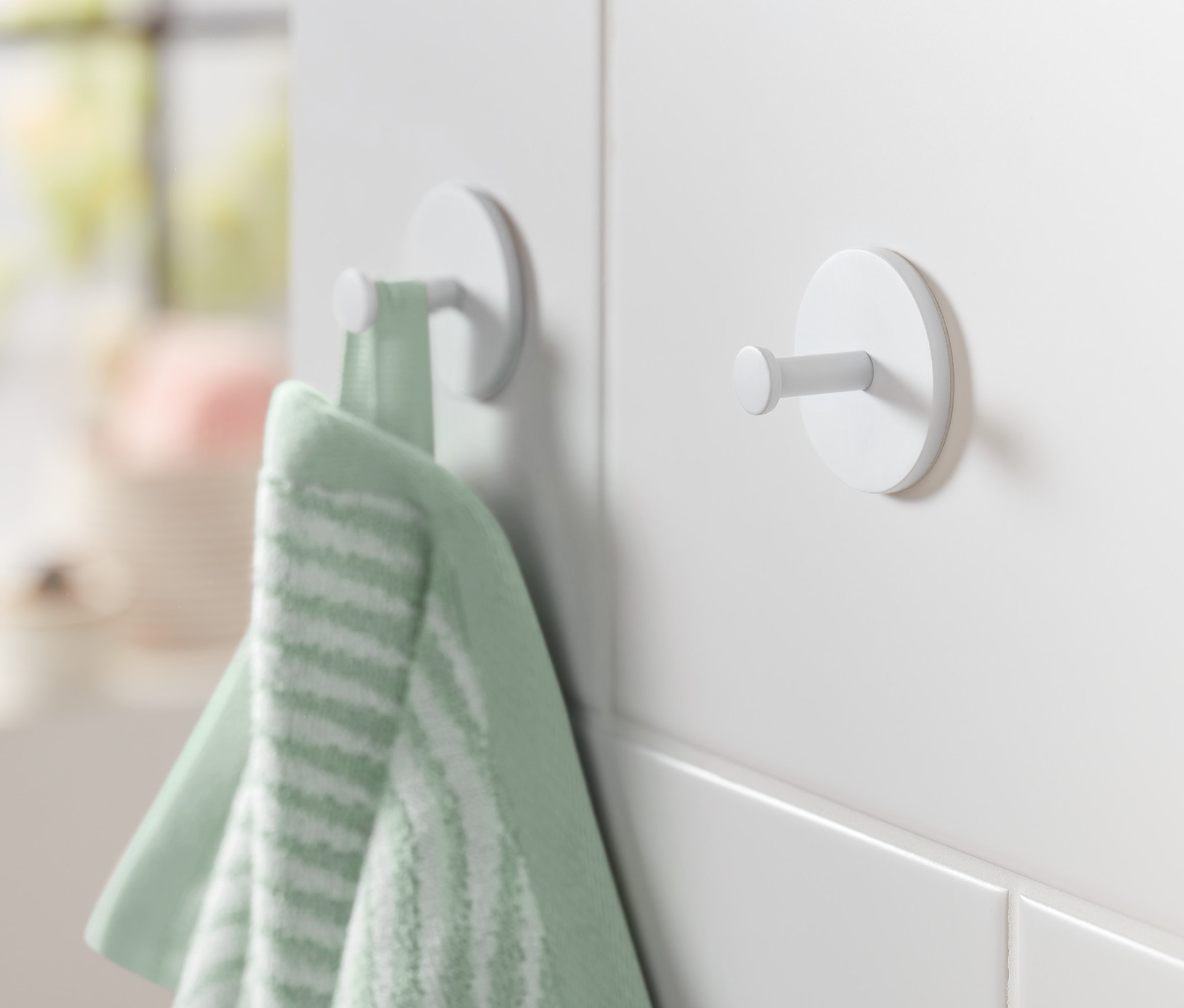 Zielony ręcznik wisi na jednym z dwóch białych haczyków przymocowanych do białej ściany.