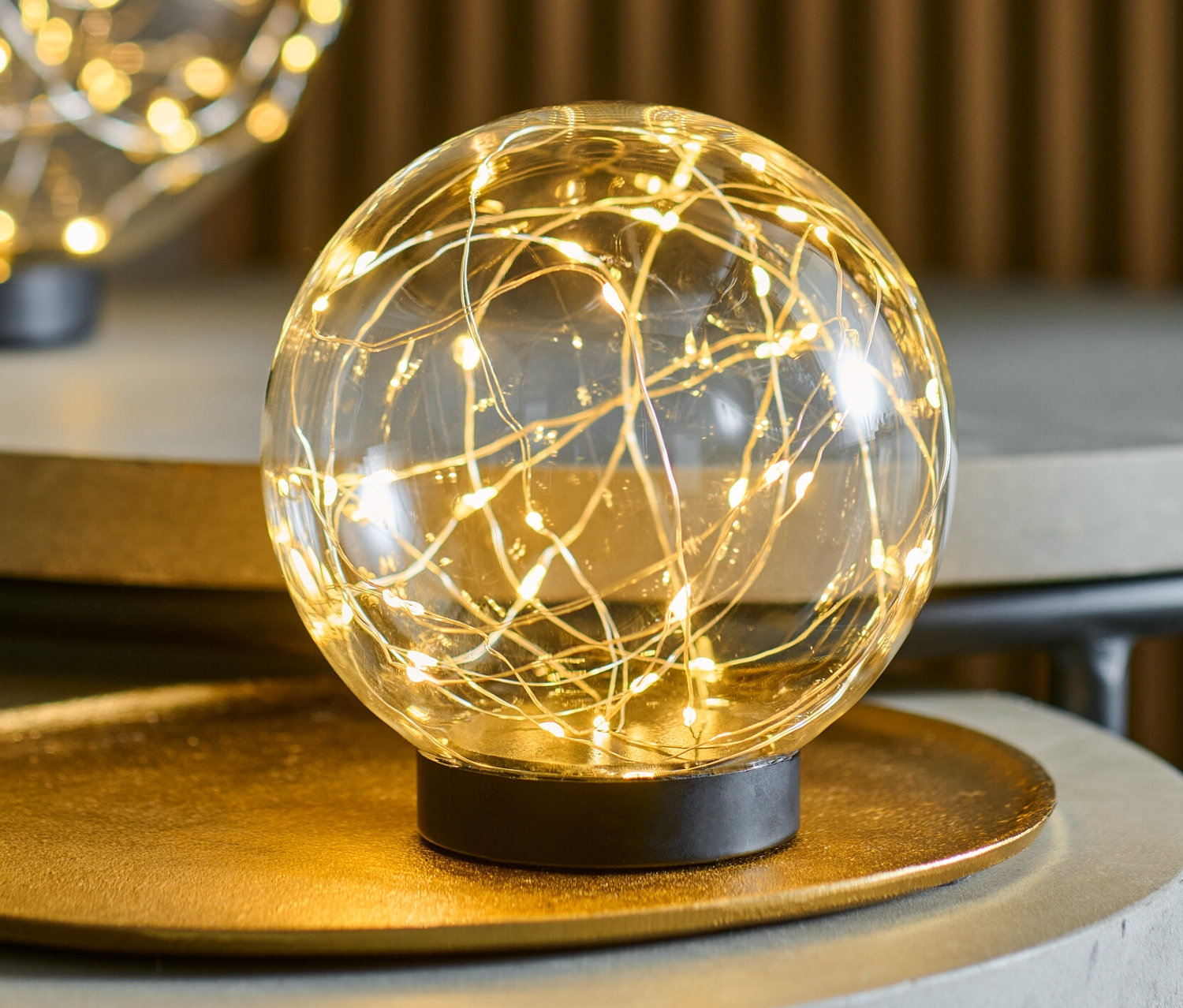 Dwie szklane kule LED, każda o średnicy ok. 15 cm, stoją na szarych stolikach.