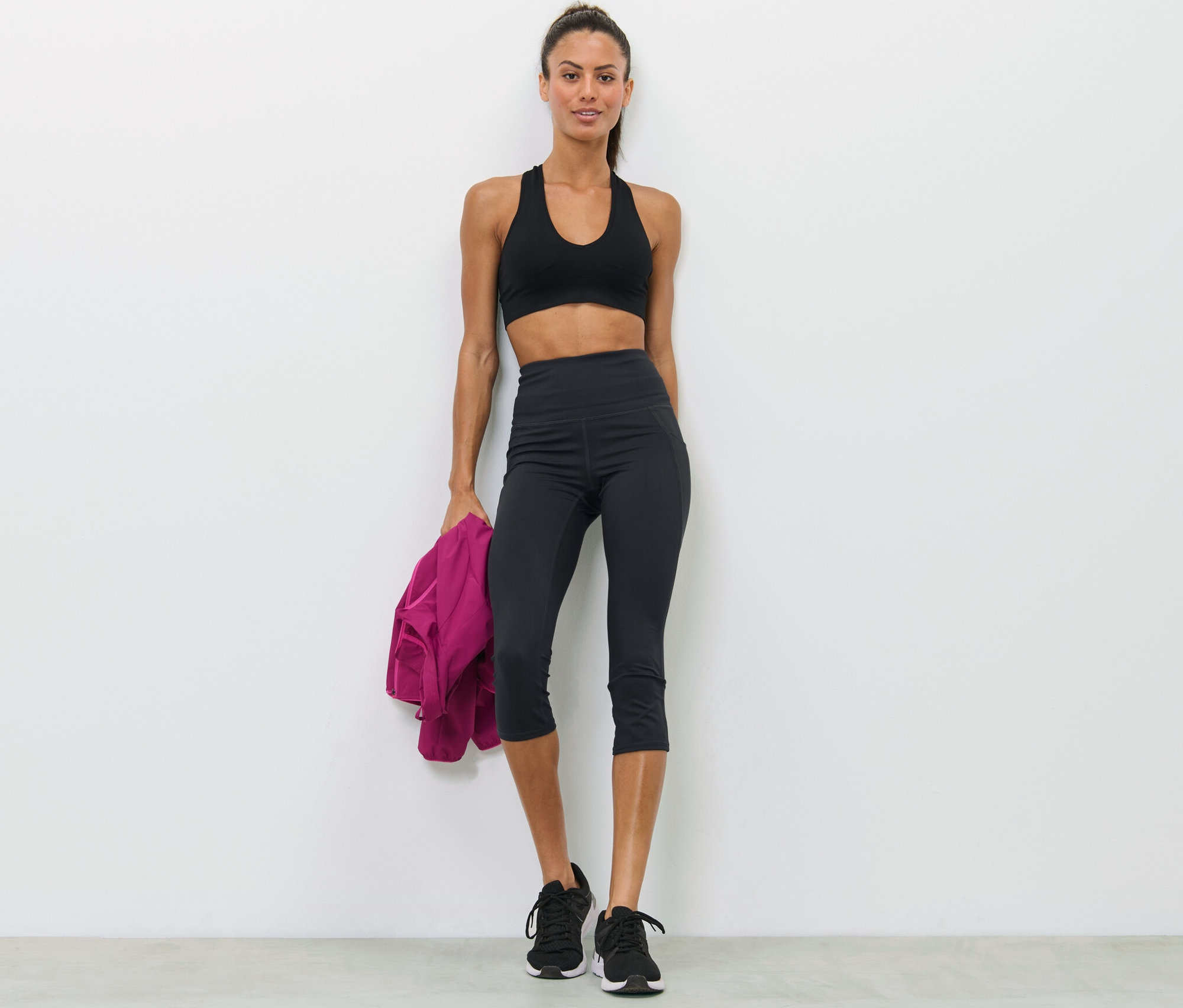 Kobieta pozuje w staniku sportowym i czarnych legginsach sportowych o długości 3/4.