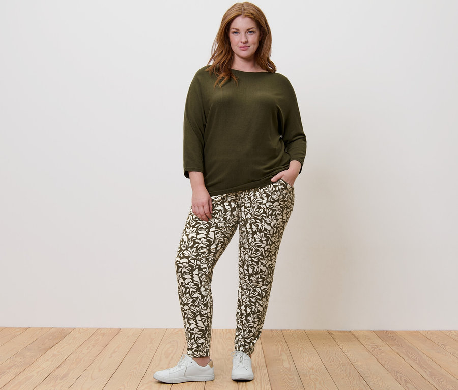 Kobieta stoi, ubrana w zielony sweter z delikatnej dzianiny i spodnie z dżerseju z nadrukiem.