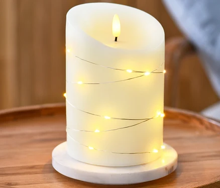 Świeca LED z prawdziwego wosku z łańcuchem z mikro LED stoi na okrągłym drewnianym stole.