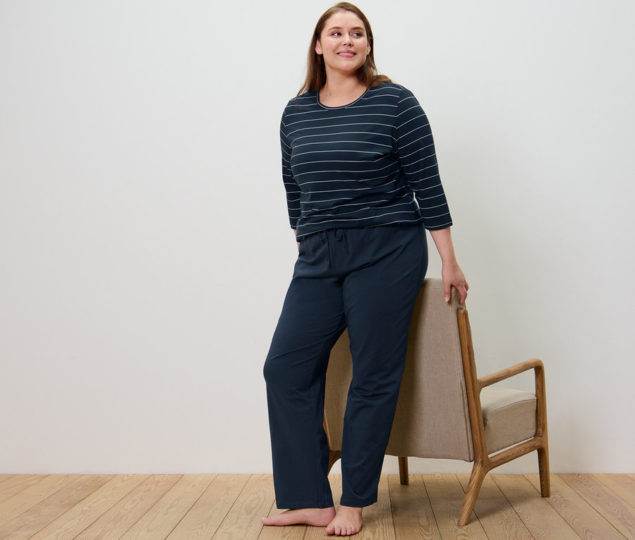 Kobieta w granatowej piżamie w paski stoi obok krzesła.