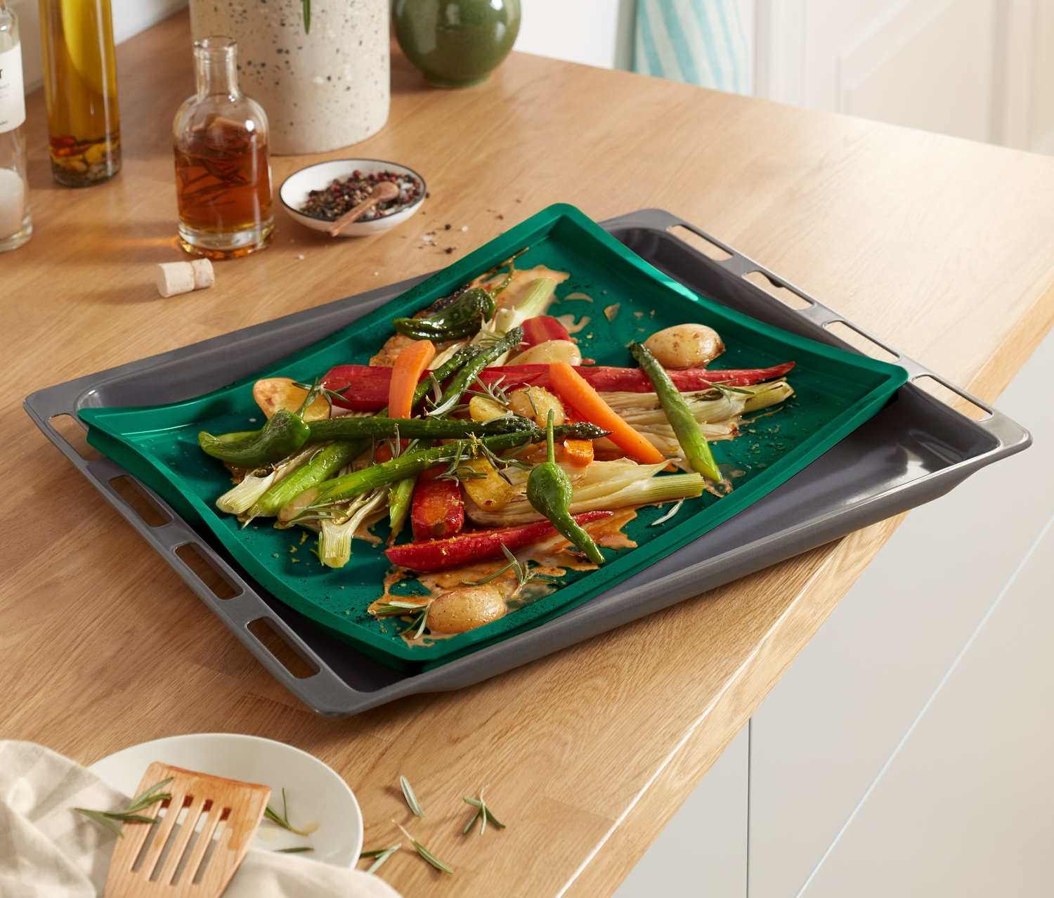 Warzywa na macie do pieczenia z podwyższonym brzegiem na blasze do pieczenia. W tle przyprawy i zioła.