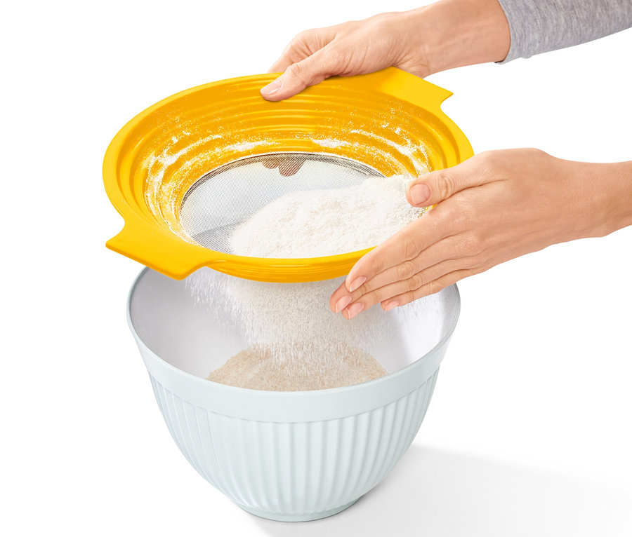 Kobieta przesiewa mąkę przez żółte sitko do przesiewania mąki i przecierania 2 w 1 do miski.