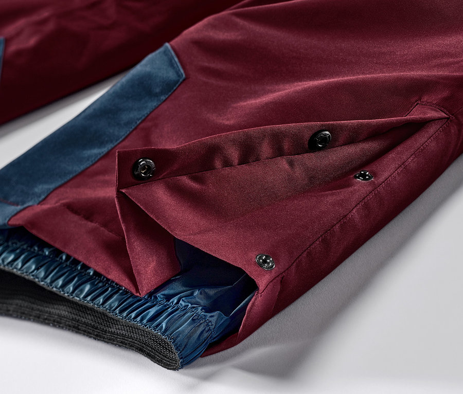 Zbliżenie na bordowe spodnie narciarskie i snowboardowe z niebieskimi akcentami i zapięciem na guziki.