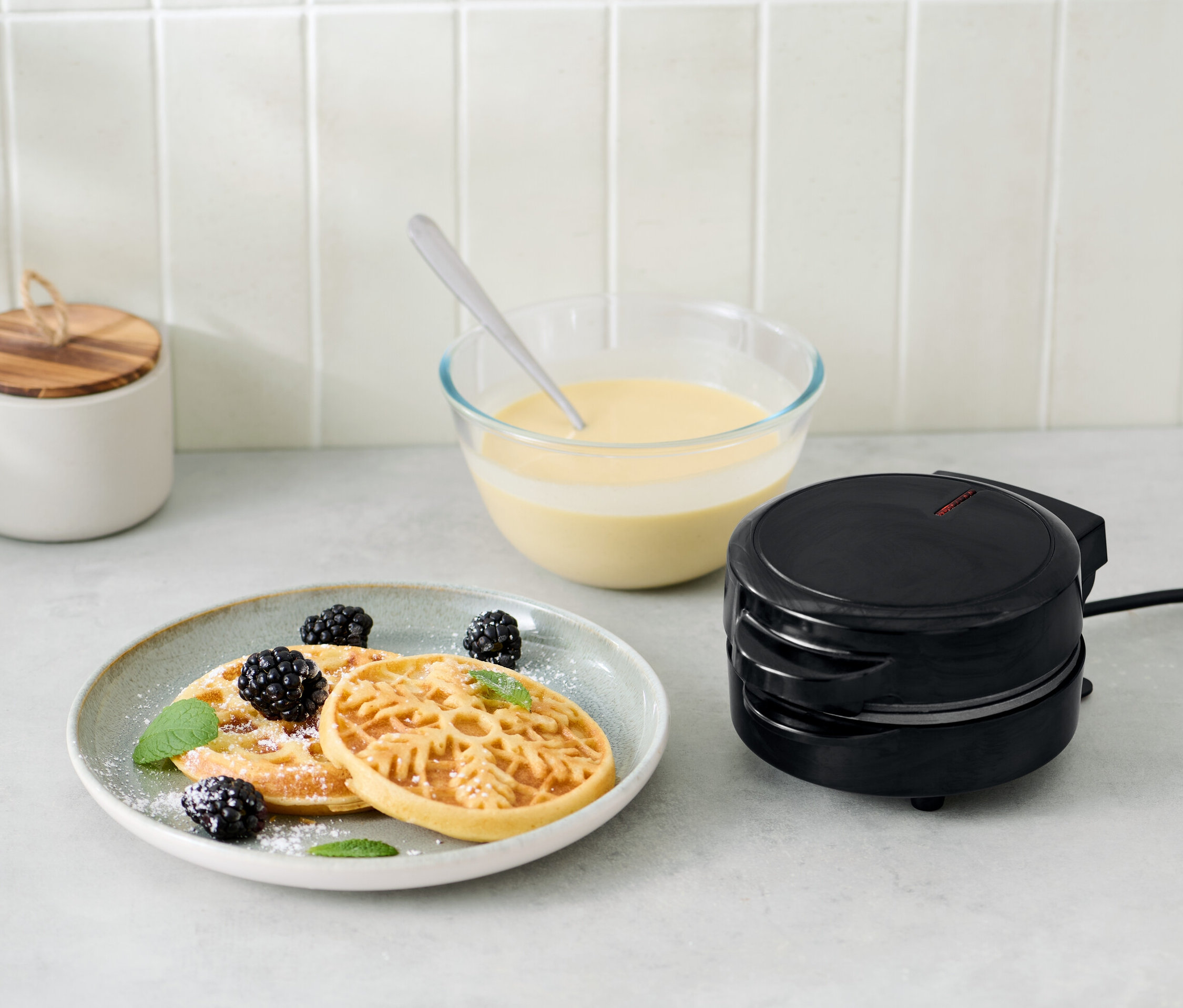 Gofrownica do minigofrów obok talerza z goframi, jeżynami i miętą.