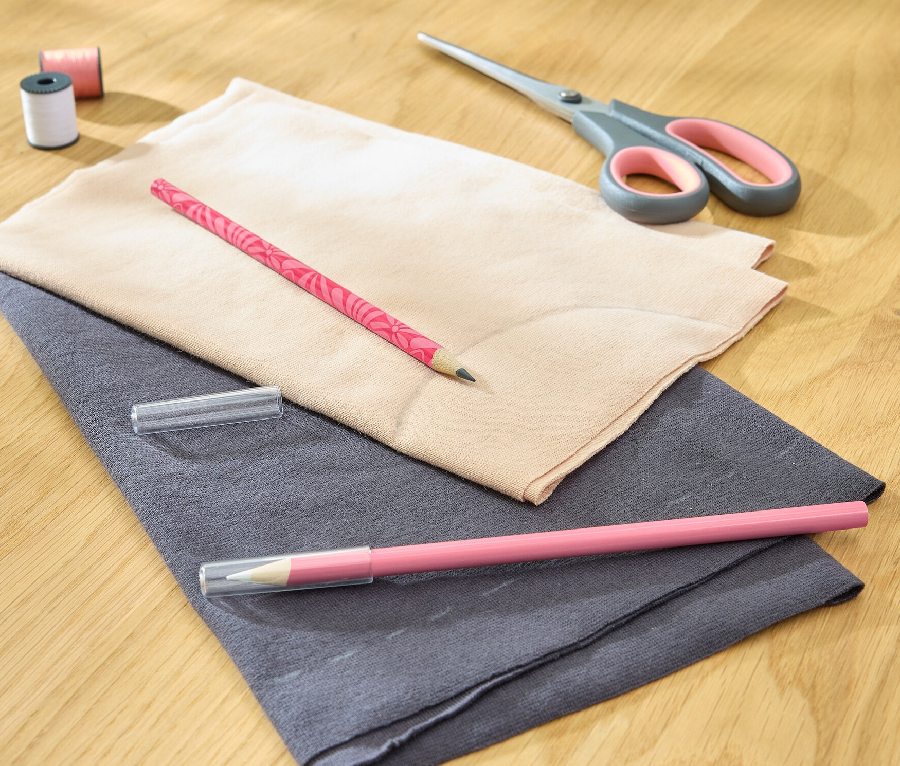 Dwa pisaki kredowe do tkanin leżą na tkaninie z nożyczkami, nicią i szpulką.