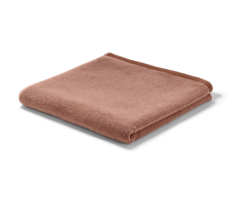 Żakardowy ręcznik kąpielowy wysokiej jakości w kolorze różowo-rdzawej czerwieni złożony na białym tle.