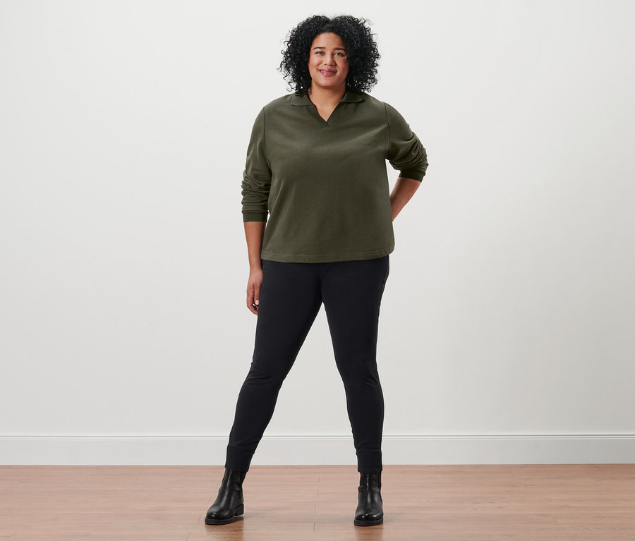 Kobieta pozuje w bluzie z kołnierzykiem, jegginsach i skórzanych butach.