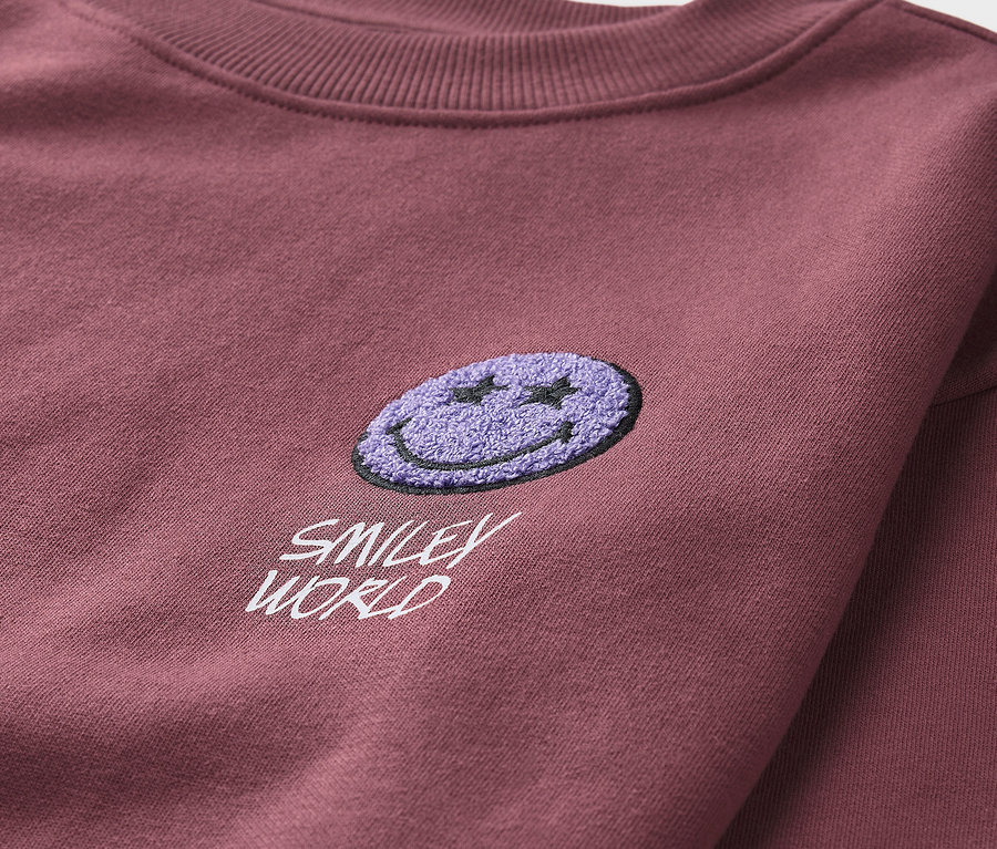 Zbliżenie na bordową bluzę dziecięcą SMILEYWORLD® z fioletową naszywką.