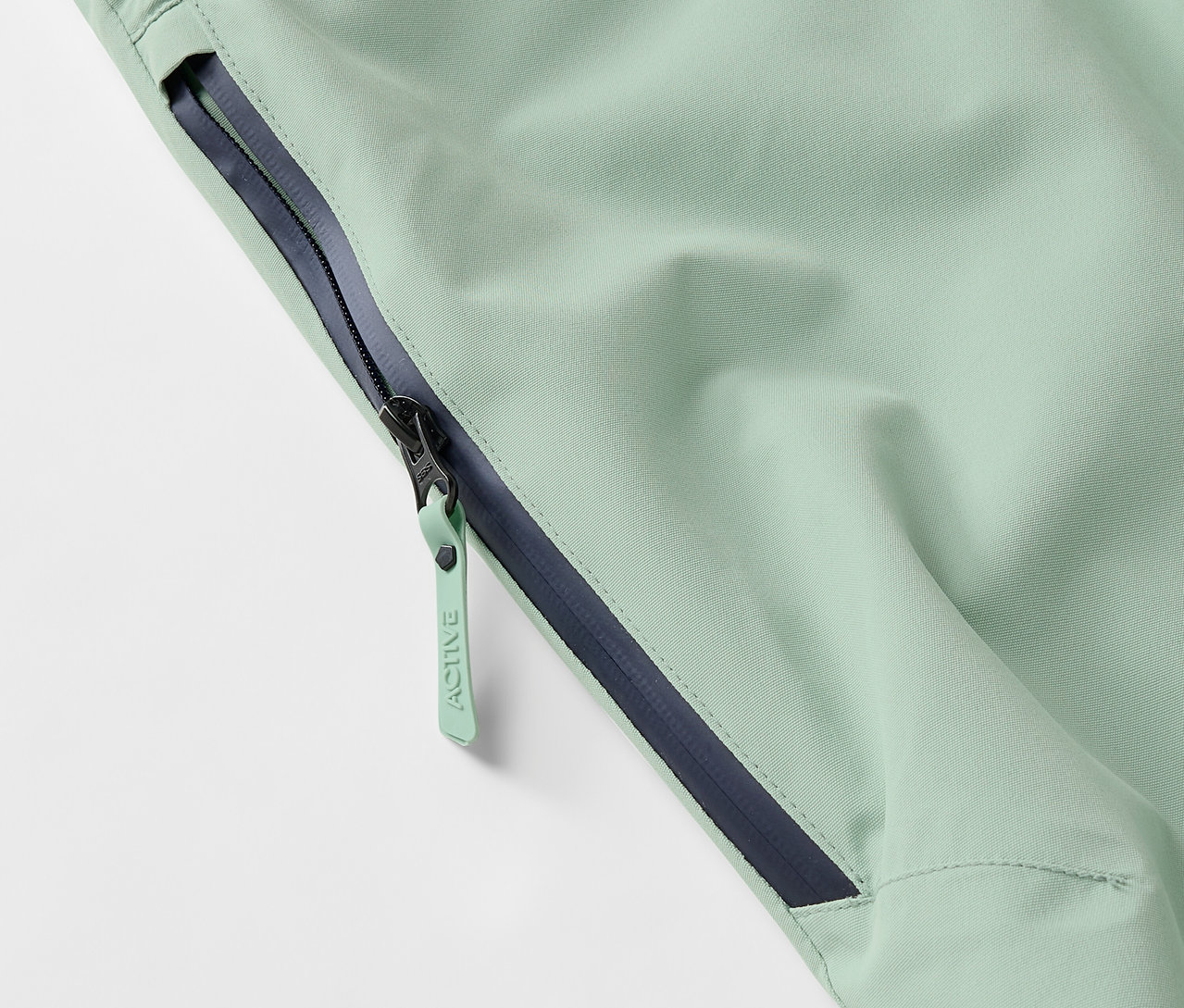 Szczegół jasnozielonej kurtki z zamkiem błyskawicznym i ciemnoniebieskim obszyciem.