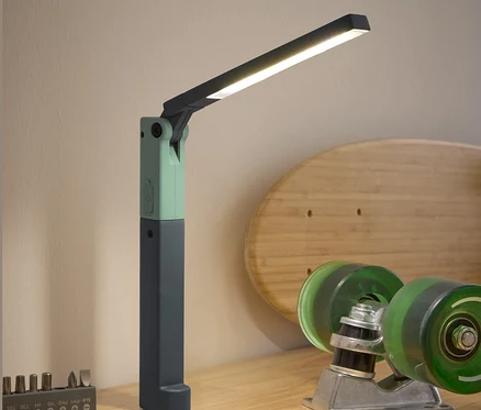 Na drewnianym stole stoi lampa robocza LED, śrubokręt, zestaw bitów i akcesoria do deskorolki.