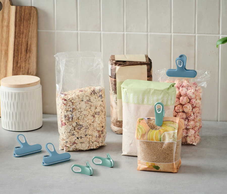 Na blacie kuchennym stoi kilka otwartych toreb z jedzeniem, zamkniętych kolorowymi klipsami.