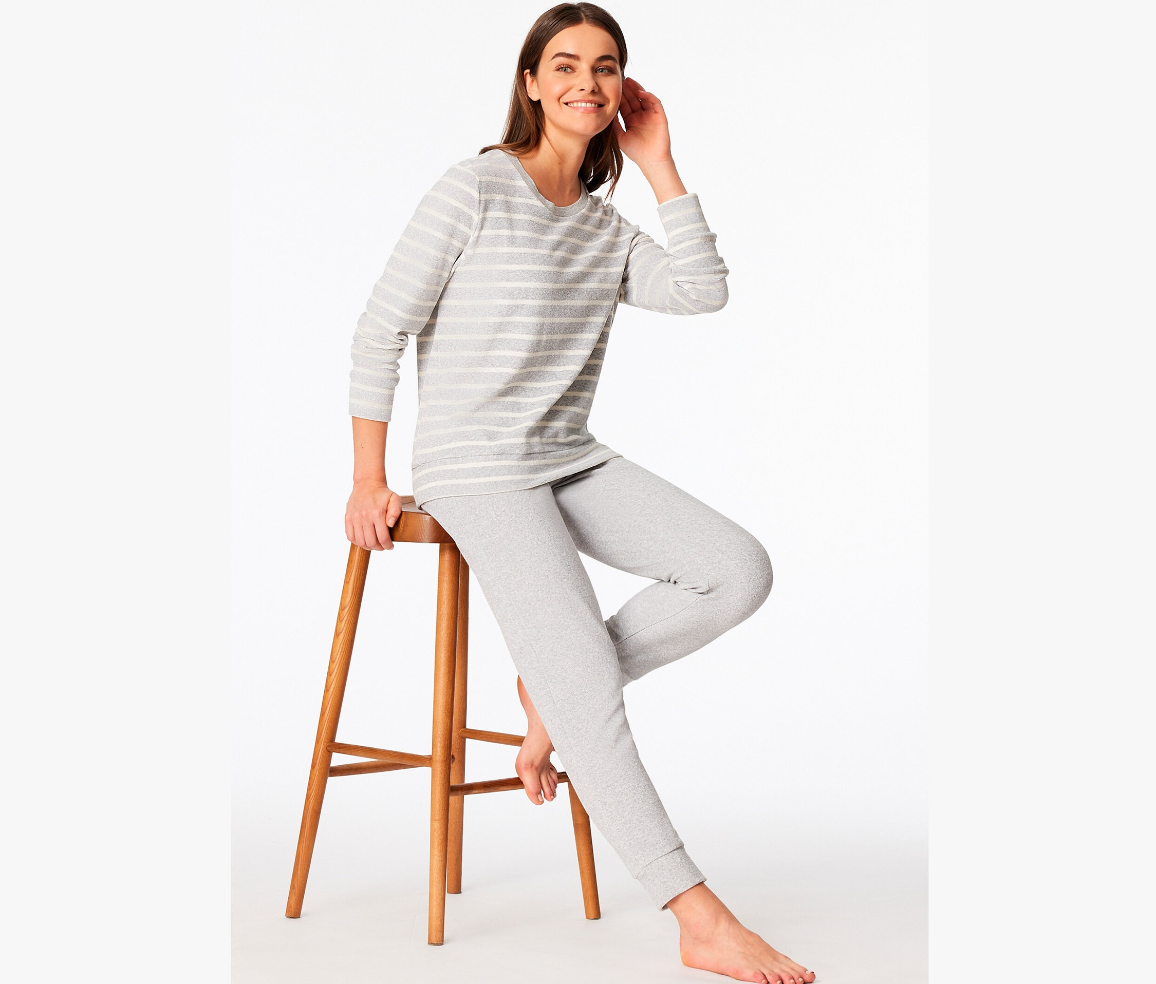 Kobieta siedzi na drewnianym stołku, ubrana w szarą piżamę w paski.