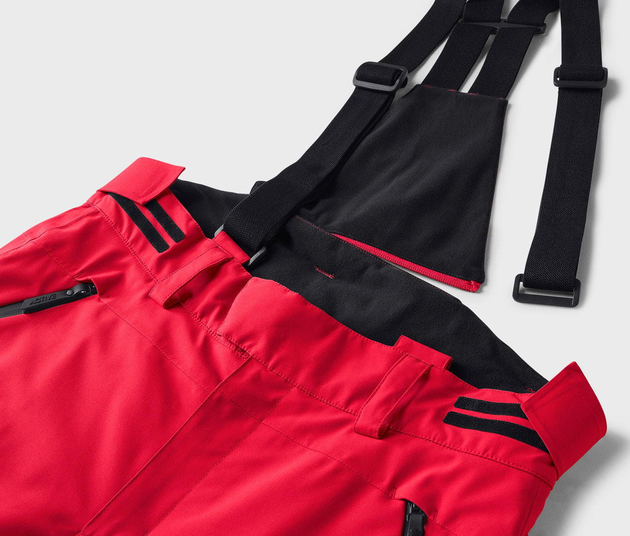 Szczegół czerwonych spodni narciarskich z czarnymi szelkami.