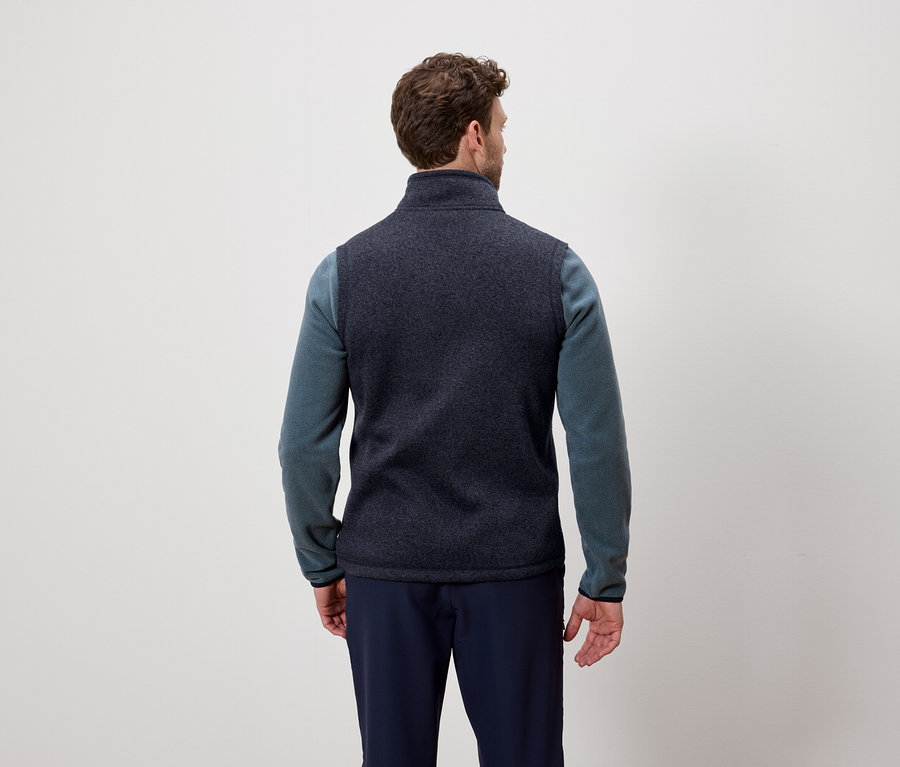 Mężczyzna tyłem do aparatu ma na sobie granatową kamizelkę i niebieski sweter.