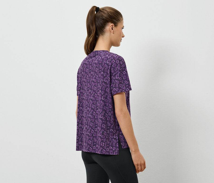 Kobieta ma na sobie fioletową koszulę z krótkim rękawem i czarne legginsy.