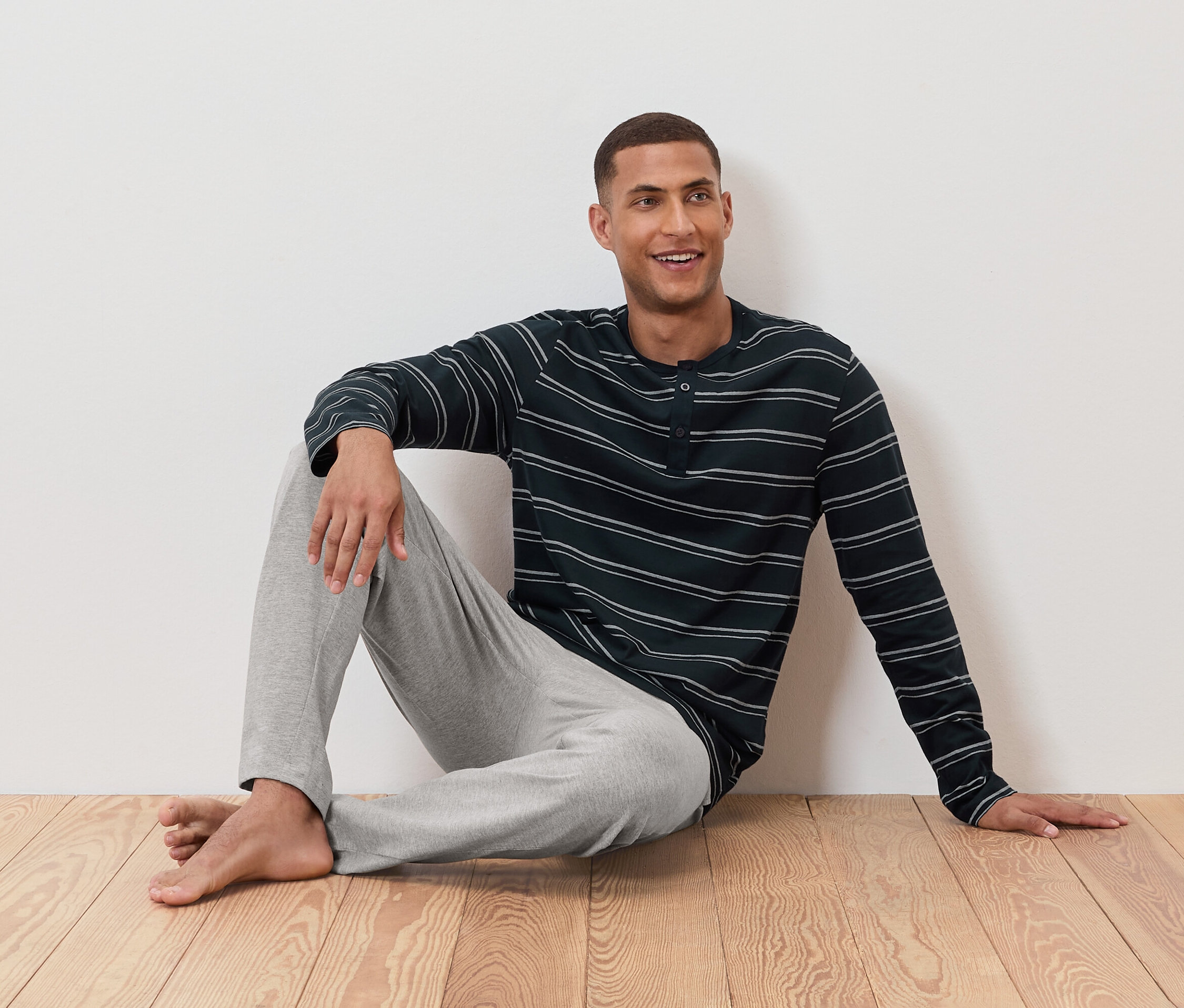 Mężczyzna siedzi na podłodze w piżamie w paski i szarych spodniach.