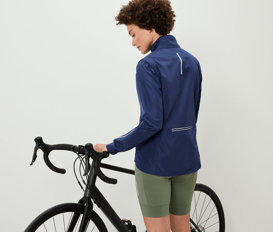 Kobieta stoi obok roweru i ma na sobie kurtkę rowerową 2 w 1.
