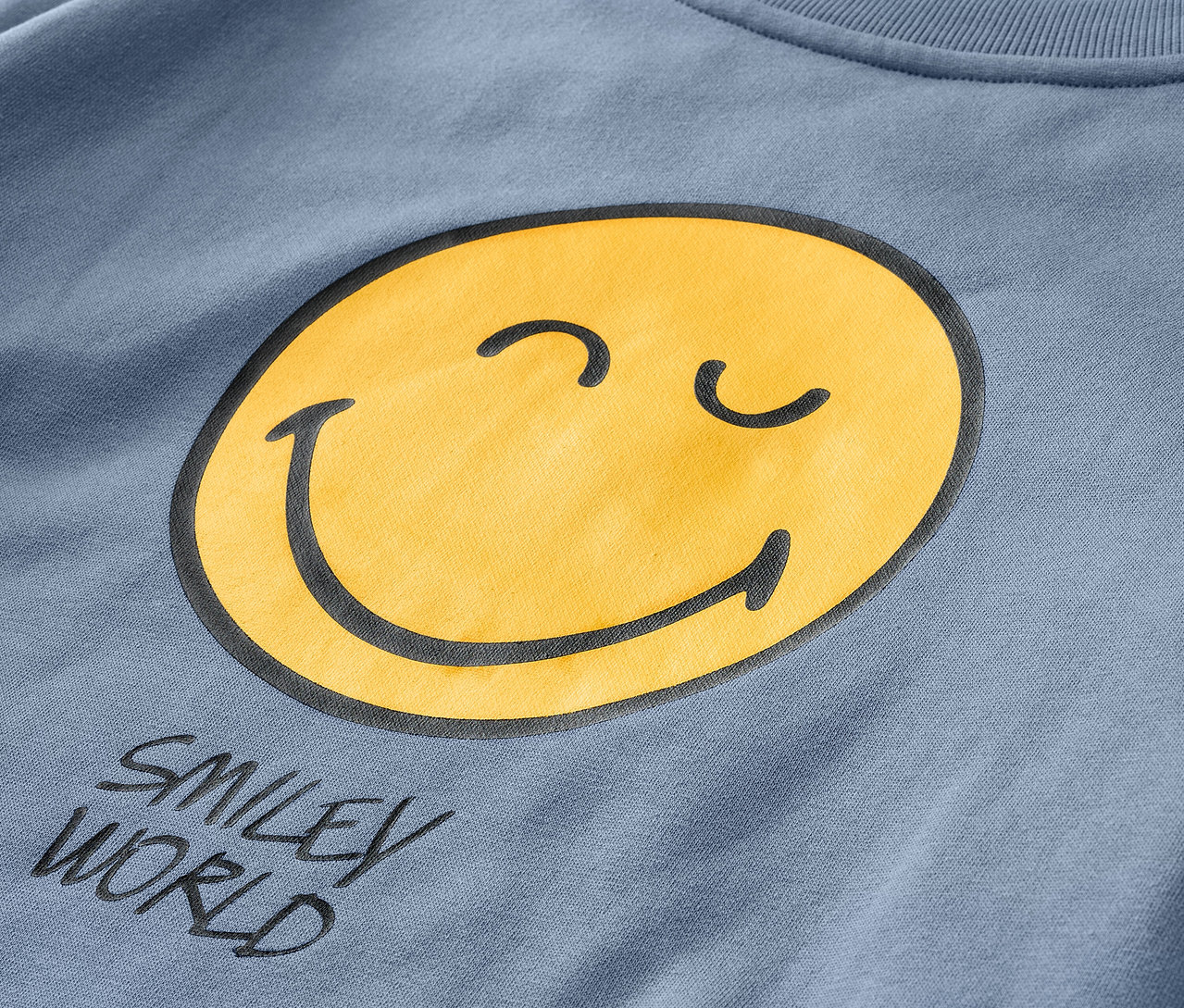 Zbliżenie na niebieską bluzę dziecięcą SMILEYWORLD® z żółtą buźką.