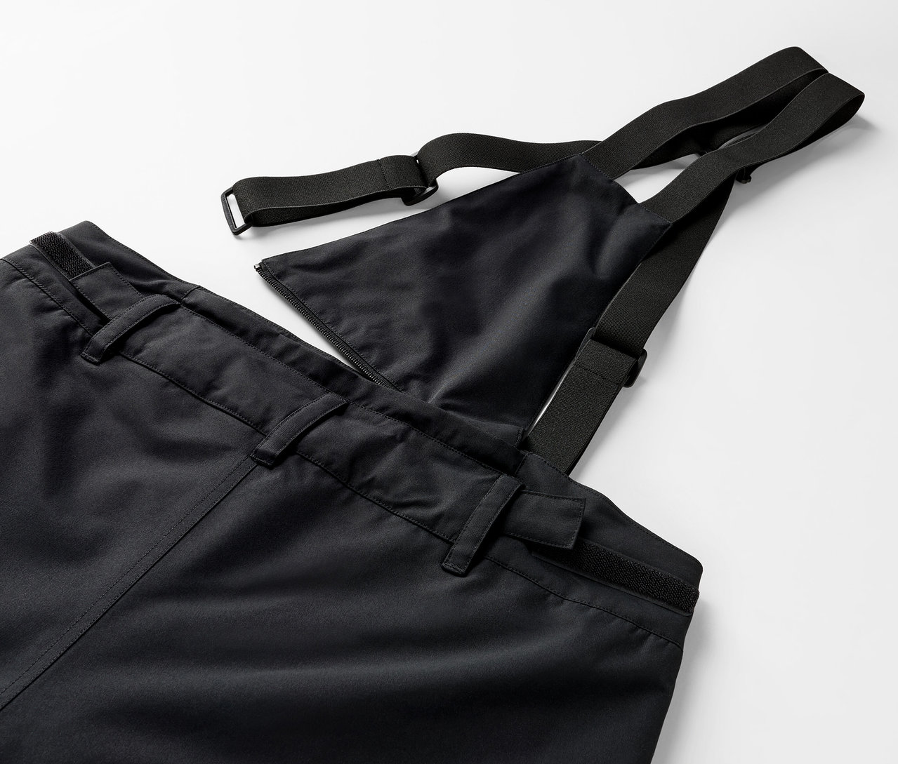 Szczegół czarnych spodni na szelkach z elastycznymi ramiączkami.