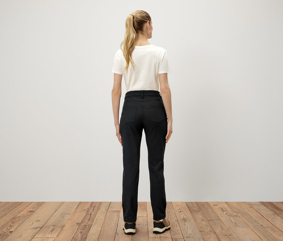 Widok z tyłu kobiety z blond włosami związanymi w kucyk, ubranej w białą koszulkę i czarne spodnie.