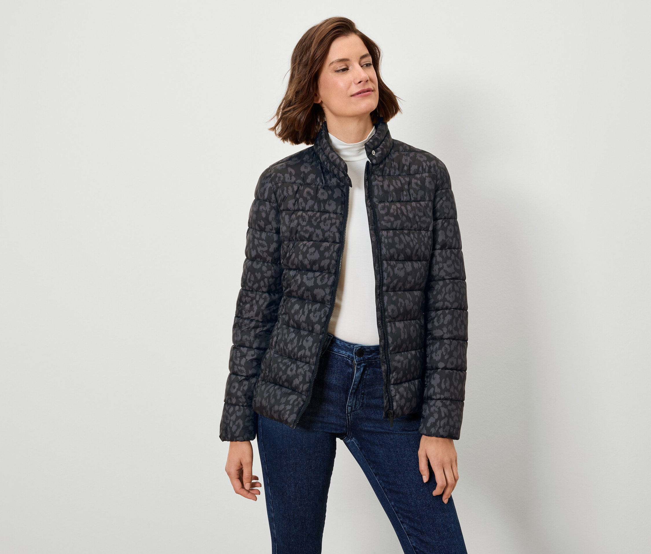 Kobieta ma na sobie czarną kurtkę puchową we wzory i dżinsy.