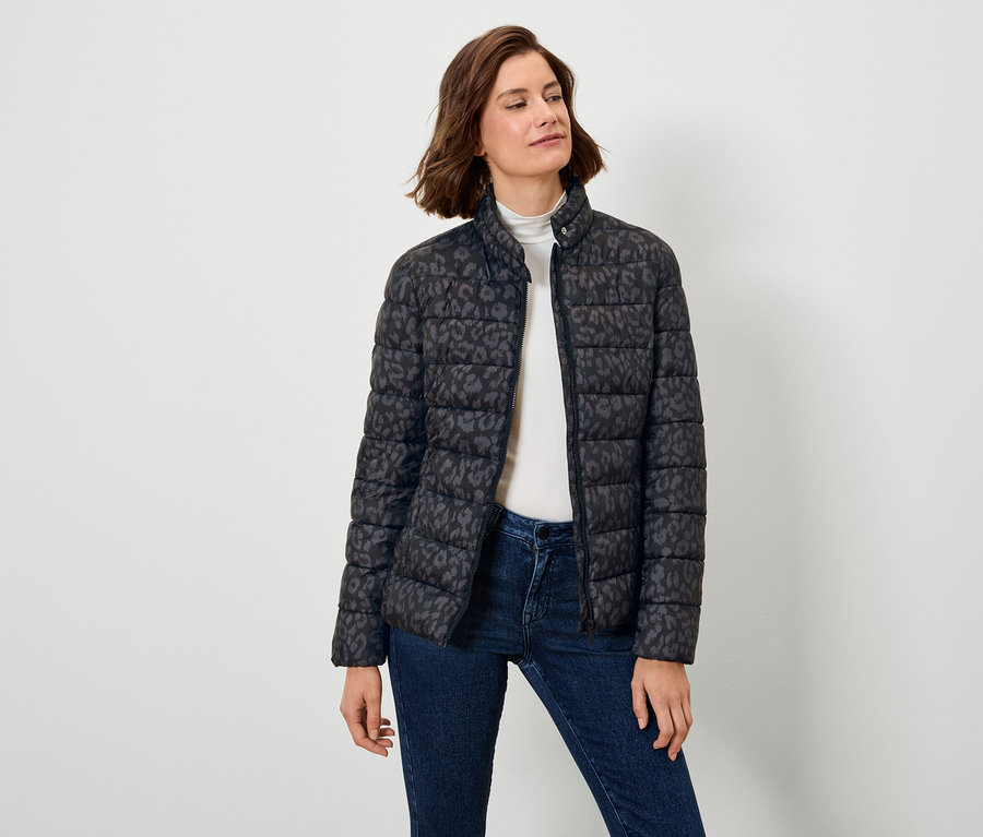 Kobieta ma na sobie czarną kurtkę puchową we wzory i dżinsy.