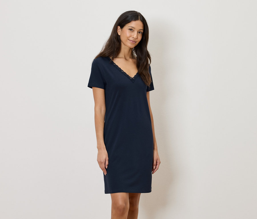 Kobieta ma na sobie granatową sukienkę do kolan z koronkowym wykończeniem przy dekolcie w kształcie litery V.