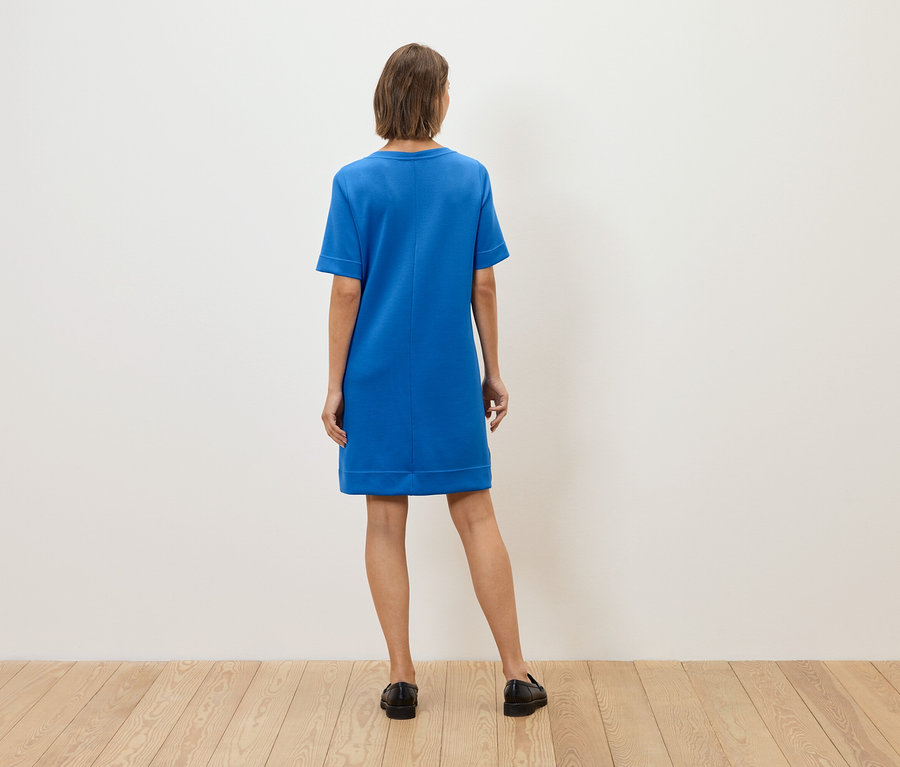 Kobieta tyłem do kamery ma na sobie niebieską sukienkę i czarne buty.