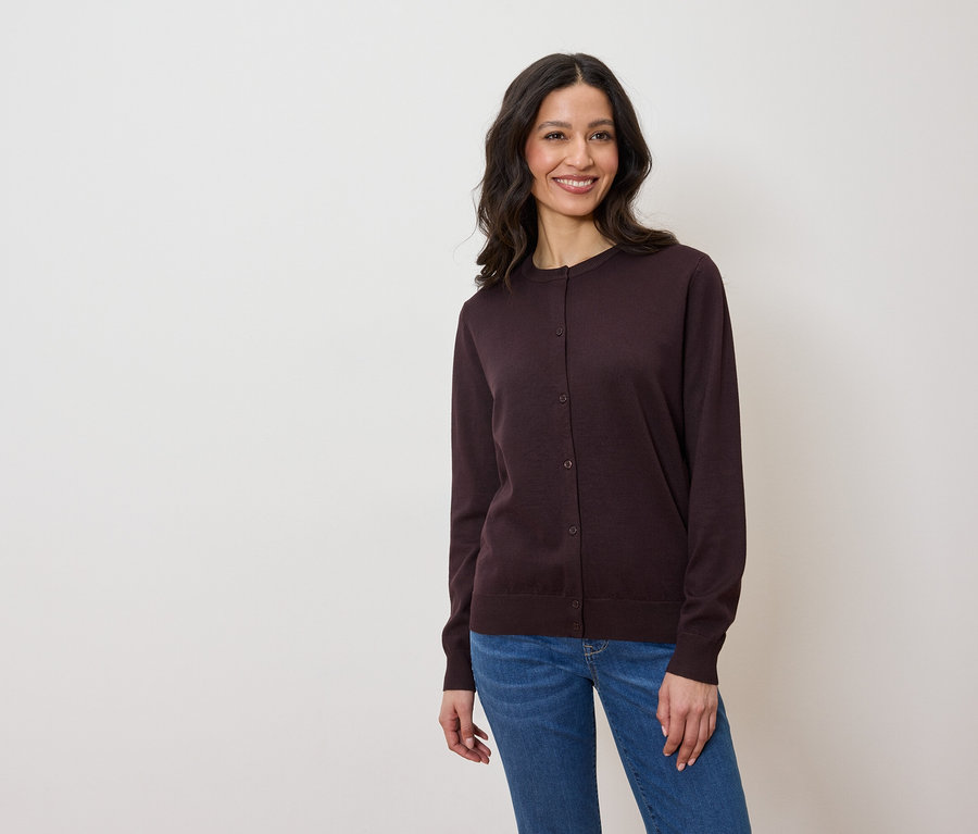 Kobieta ma na sobie ciemnofioletowy kardigan i dżinsy.