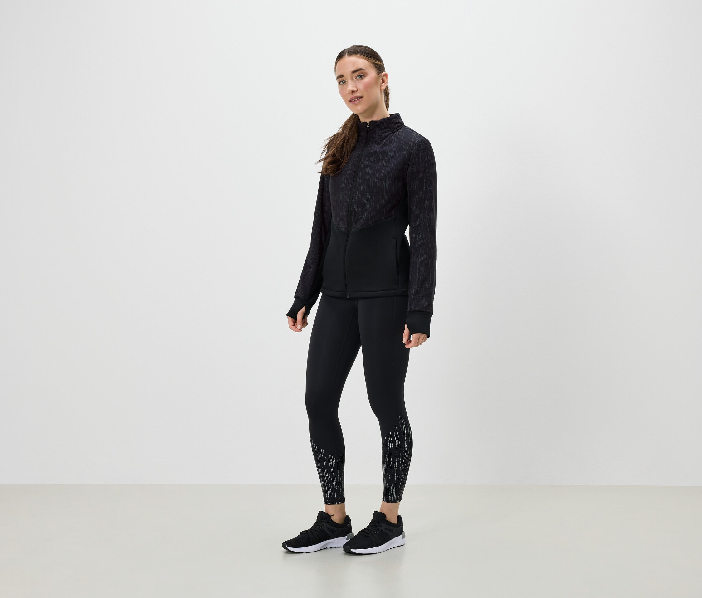 Kobieta w czarnym stroju sportowym pozuje na jasnym tle.