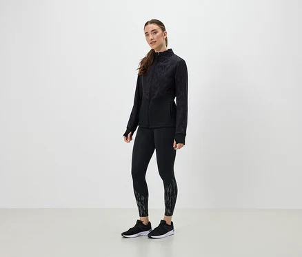 Kobieta w czarnym stroju sportowym pozuje na jasnym tle.