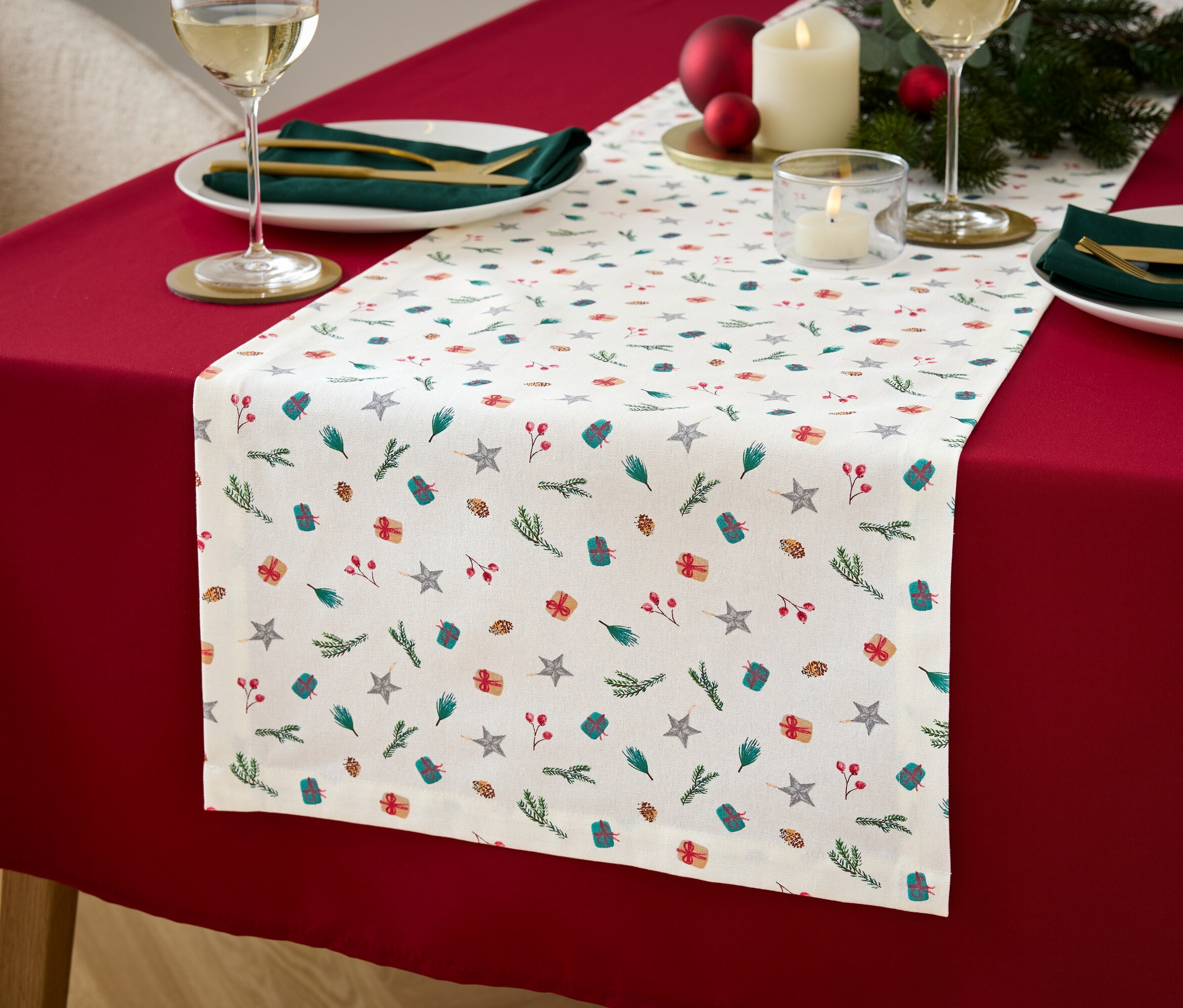 Stół nakryty czerwonym obrusem i białym bieżnikiem we wzory gwiazd, prezentów i gałązek.