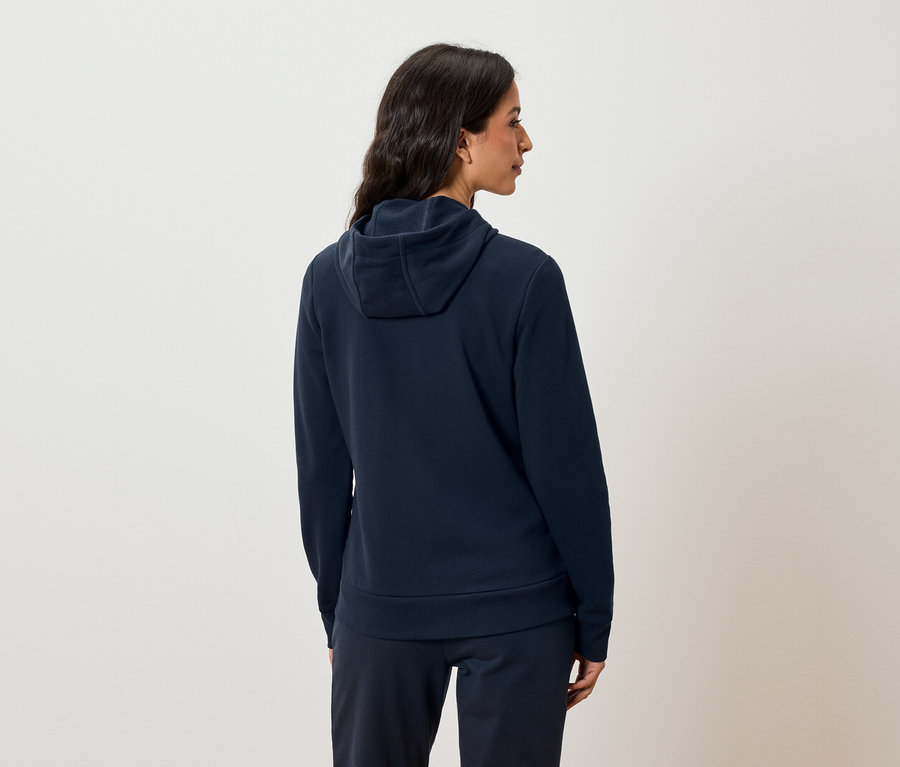 Kobieta tyłem do aparatu ubrana w granatową bluzę z kapturem i spodnie dresowe.