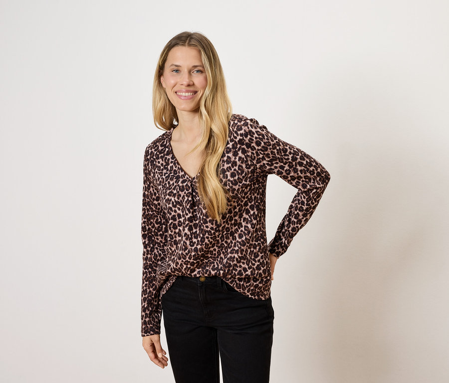 Kobieta z długimi blond włosami pozuje w bluzce we wzór zwierzęcy i czarnych spodniach.