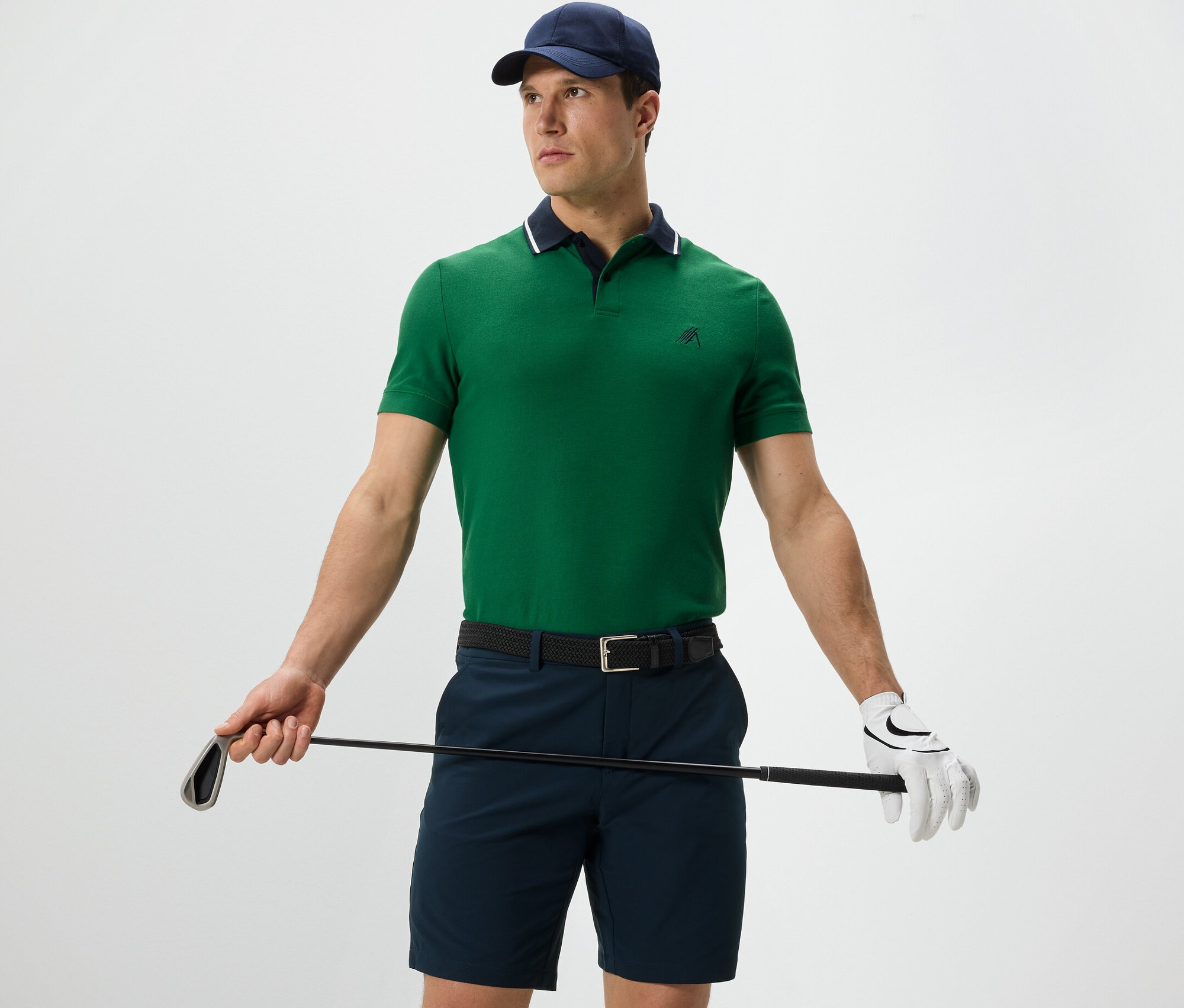 Mężczyzna trzyma kij golfowy i ma na sobie zieloną funkcyjną koszulkę polo.