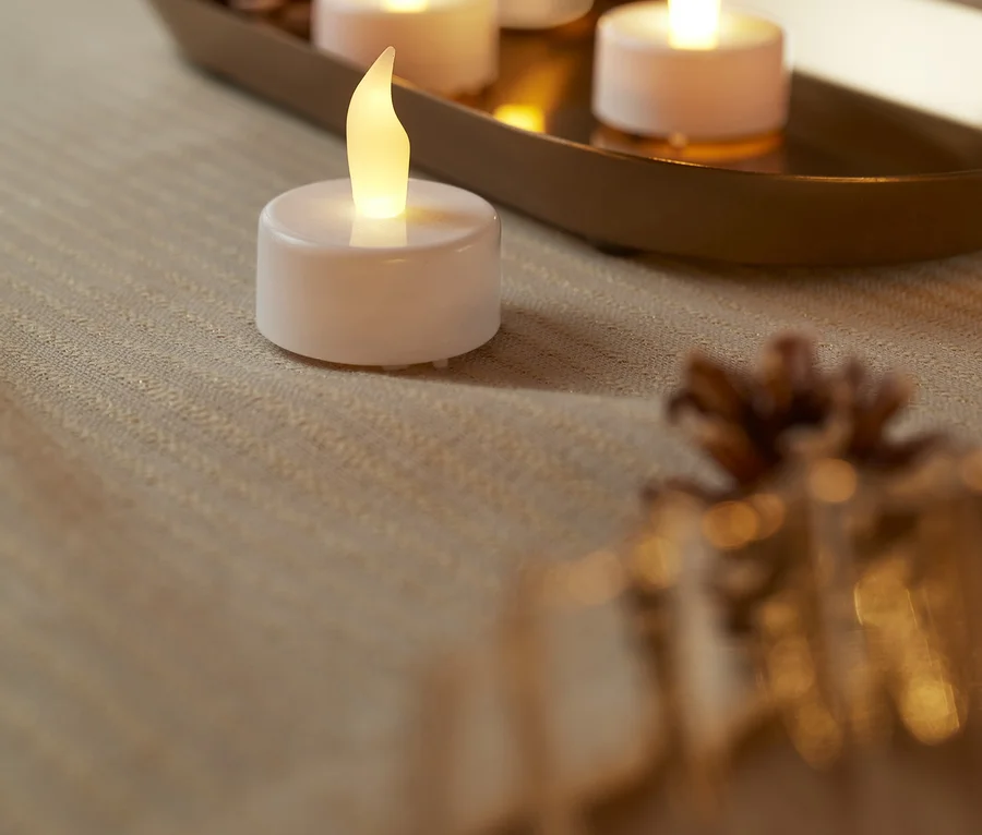 Cztery białe świeczki typu tea light z diodami LED na stole.