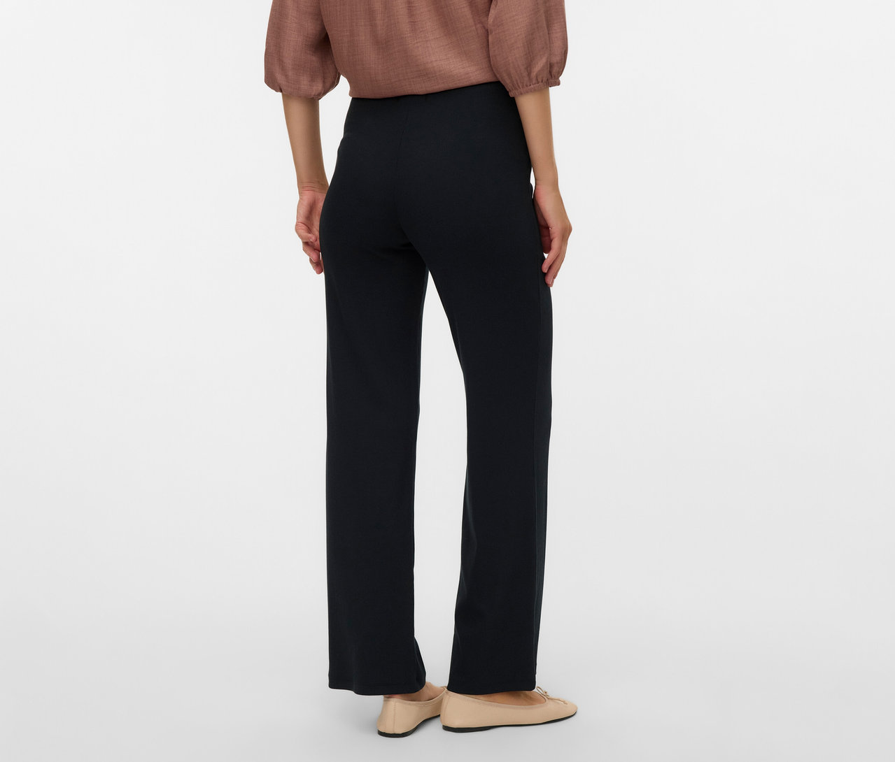 Widok z tyłu kobiety w brązowej bluzce i czarnych, luźnych legginsach ciążowych MAMALICIOUS „MLEMILY” oraz beżowych balerinach.