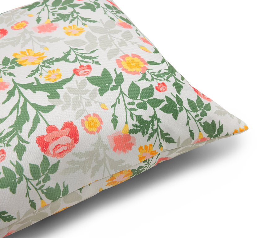 Zbliżenie poduszki z kwiatowym wzorem w odcieniach czerwieni, żółci i zieleni na białym tle.