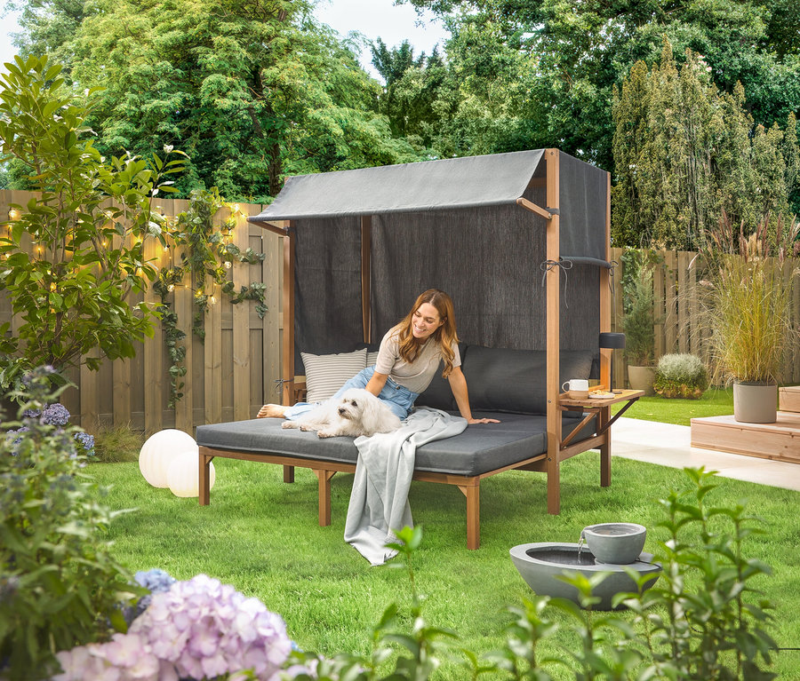 Kobieta siedzi z psem na solarnej fontannie ogrodowej w ogrodzie.