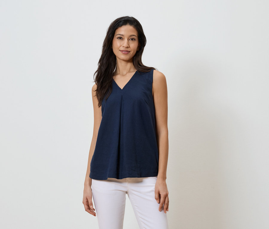 Kobieta ma na sobie granatowy top bez rękawów z dekoltem w szpic i białe dżinsy.
